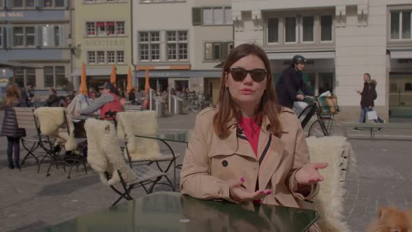 Woman Speaks Sitting at the Table of a Street Cafe