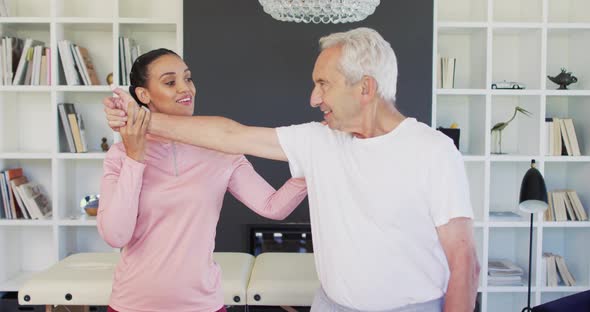 Video of happy biracial female physiotherapist exercising with caucasian senior man