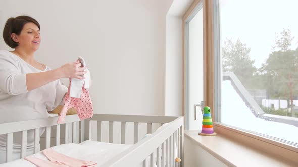 Happy Pregnant Woman Setting Baby Clothes at Home 