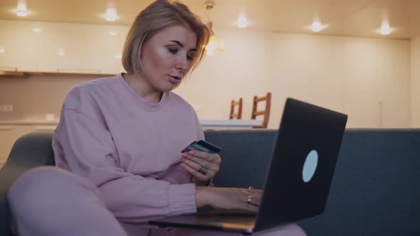 Woman Holding Plastic Card in Hands and Using Laptop