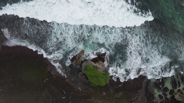 Top down aerial view of giant ocean waves crashing and foaming in coral beach