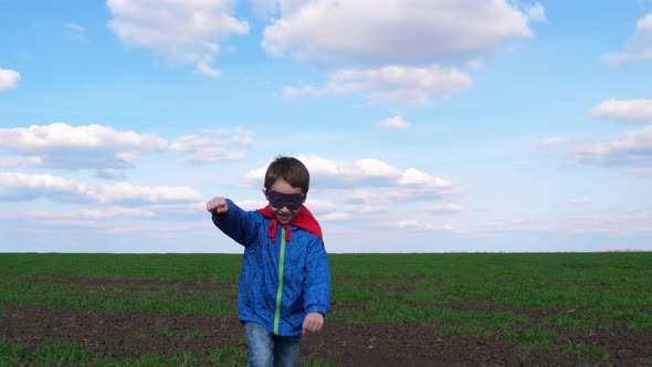 A Happy Boy in a Red Raincoat Runs Across a Meadow Against a Blue Sky