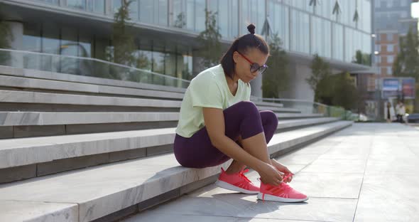 African Woman in Sportswear Tying Shoe Laces Sitting on Stairs Outdoors