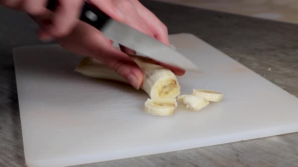 A woman in a kitchen cutting up a banana on a plastic chopping board fruit salad healthy eating