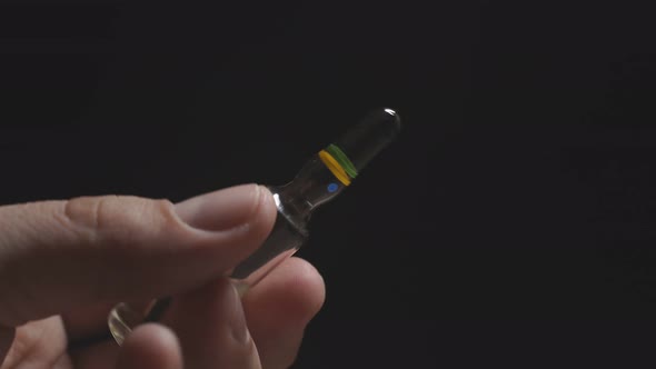 Close-up of a Man's Hand on a Dark Background Holding an Ampoule for Injection. Coronavirus