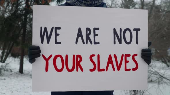 Person is standing and holding a White Sign that says We Are Not Your Slaves.