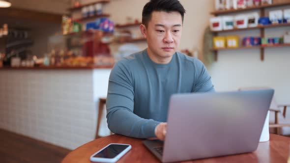 Confident Asian young man working by laptop and talking by phone