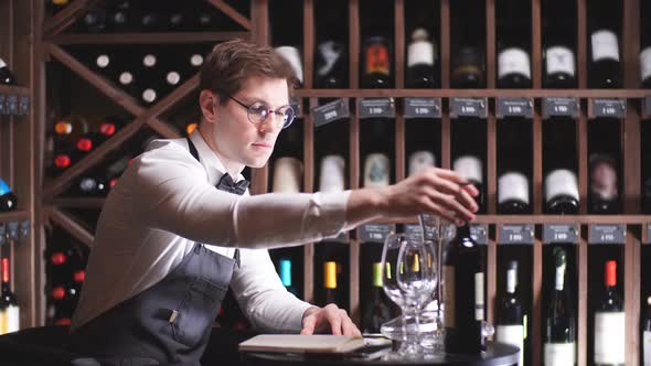 Male Cavist Examines the Bottles with Wine and Making Notes at His Notepad