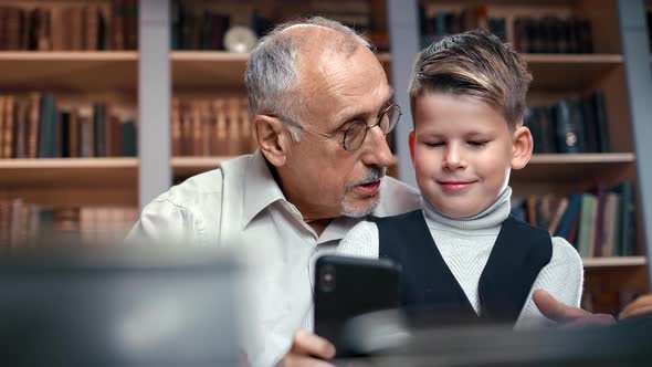 Closeup Grandfather and Grandchild Talking Discussing with Smartphone Together Sitting at Library