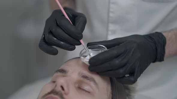 Closeup Beautician Applying White Purifying Enzyme Peel on Face of Young Caucasian Man Lying in