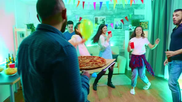 Follow Shot of Young Man Arriving at the Party with Delicious Pizza