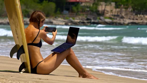 Girl Leans on Surfboard Takes Photos on Sand Beach