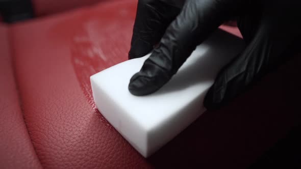 Tracking close up 4k shot of a male hand in a black rubber glove cleaning a red leather car seat usi
