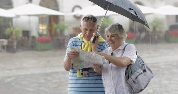 Senior Tourists in Rainy Weather Stand and Looking for the Route in Map