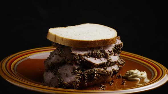 Rotating shot of delicious, premium pastrami sandwich next to a dollop of dijon mustard 