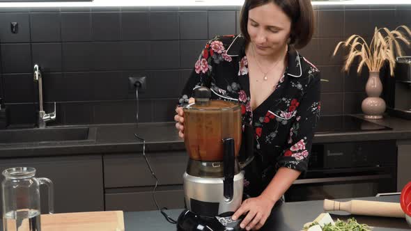 Woman mixing ingredients in blender. Female turning on blender, cooking tomato smoothie in kitchen