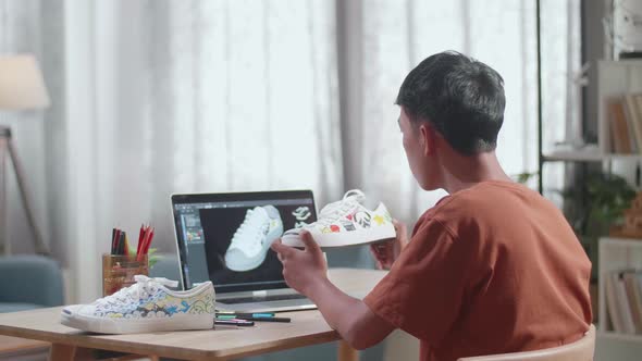 Asian Boy Footwear Designer Looking At Sneaker In Hands And Comparing It To Laptop 