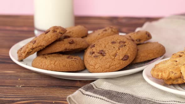 Female Hand Taking Chocolate Chip Cookie From a Plate on Wooden Table Close Up