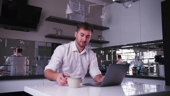young man works at a laptop and drinks coffee