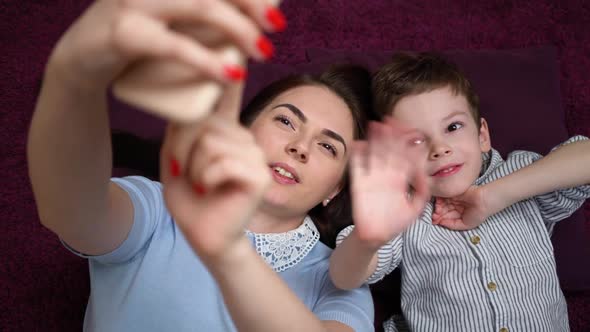 Mother and Her Son Making a Selfie or Video Call To Father or Relatives on the Carpet.