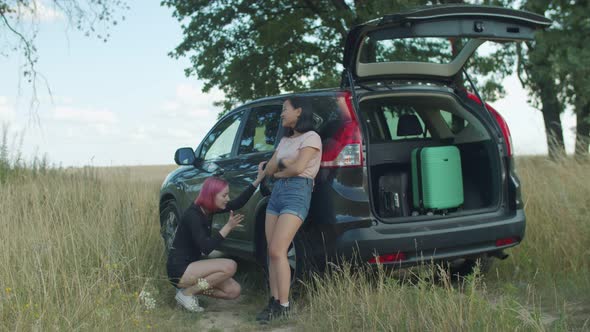 Female Travelers Checking Out Flat Tyre on Car
