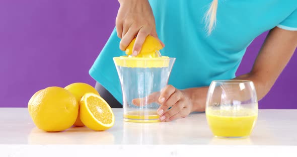 Woman preparing sweet lime juice from juicer against violet background