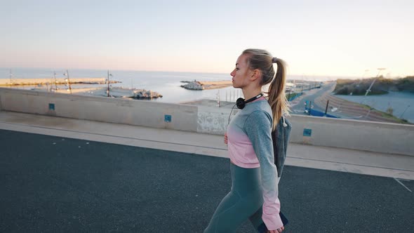 Young Female in Sportswear Walk Along Harbor at Coastal City