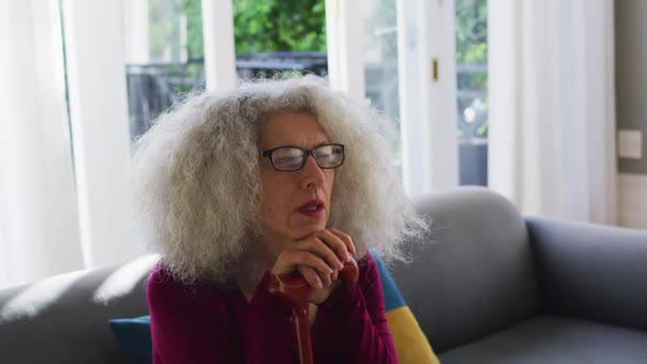 Senior caucasian woman holding walking stick while sitting on the couch at home