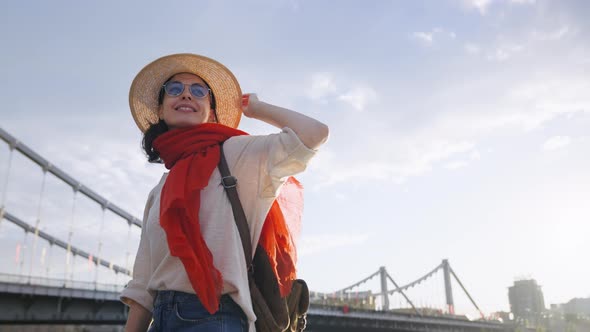 Beautiful girl in a hat on the embankment near the bridge in summer