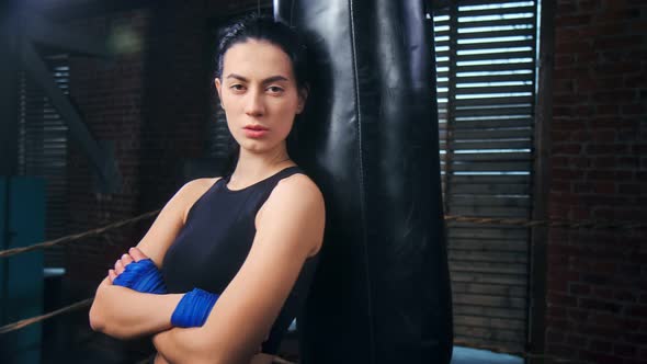 Fierce Young Asian Female Kickboxer Posing Near Punching Bag Looking at Camera Medium Shot