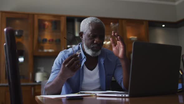 Stressed african american senior man using laptop and calculating finances at home