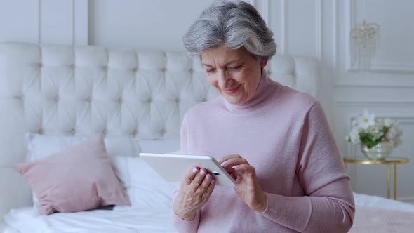 Elderly Woman Using a Tablet Gadget at Home