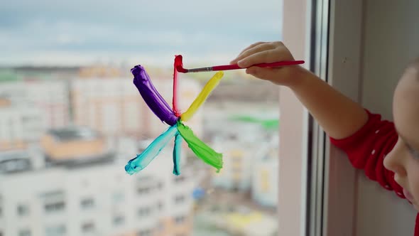 Child draw snowflake in rainbow colours on window with paints. Caucasian female person decorate room