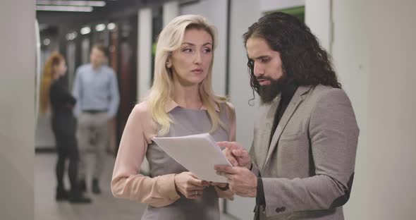 Confident Caucasian Woman and Middle Eastern Man Standing in Open Space Office with Papers and