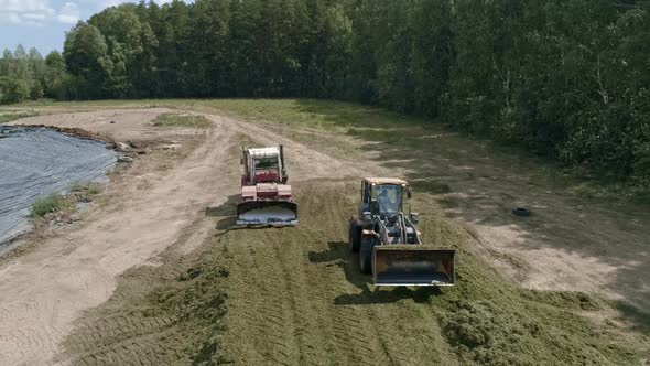 Drone view of tractors tamp the silage in the Silo Trench next to the forest 07