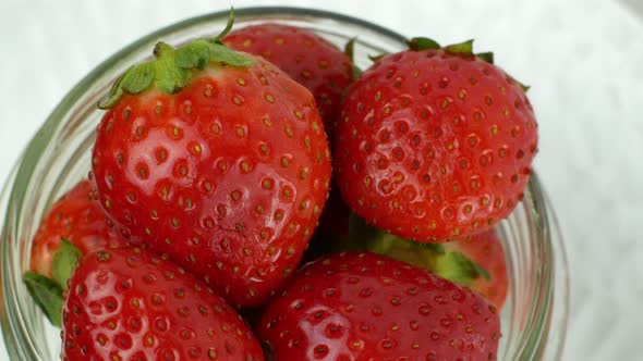 Glass jar with red ripe strawberries rotating on a white background. Ripe summer red strawberry