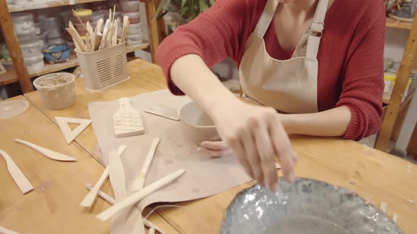 Young Female Crafter Smoothing Walls of Clay Bowl with Moist Hand