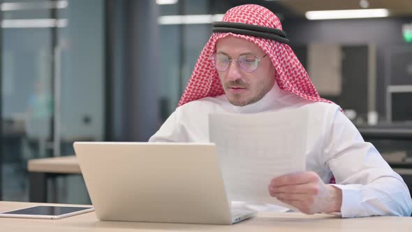 Middle Aged Arab Man with Laptop Reading Documents