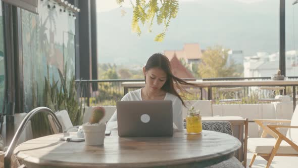 A Young Asian Girl Works at Her Laptop in a Rooftop Cafe in the City