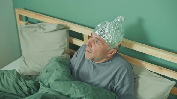 A Paranoid Man with a Protective Foil Cap On His Head Lying in Bed