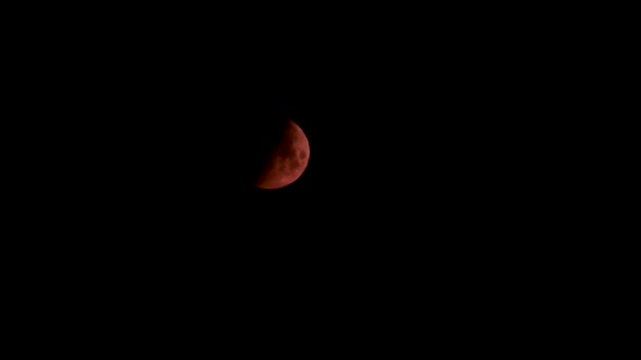 Half red moon on black sky going down video