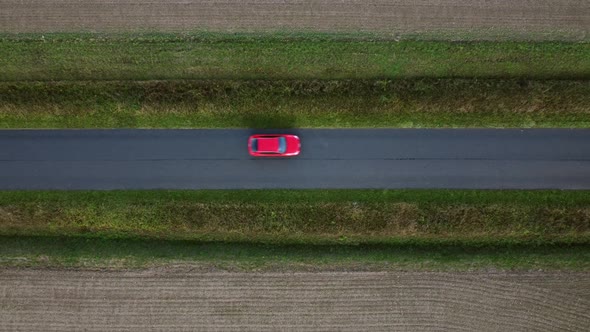 Red car drives horizontally along country road off camera