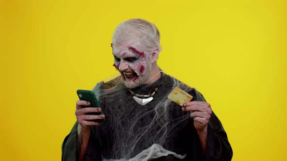 Sinister Man Halloween Zombie Using Credit Bank Card and Smartphone While Purchases Online Shopping