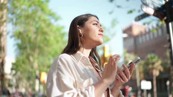 Concentrated brunette woman in headphones looking around and texting on phone