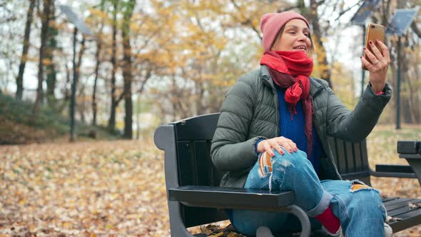 A Young Woman Talking on a Video Call on Her Smartphone While in the Autumn Park