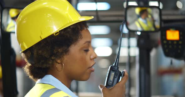 Side View of Afroamerican Woman Sitting in Forklift Using Walkietalkie Moving Goods in Warehouse