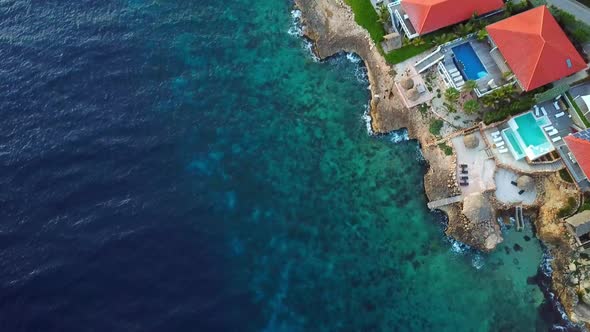 Overhead dolly-in aerial view of mansions on the shore of Jan Thiel Beach, Curacao, Dutch Caribbean