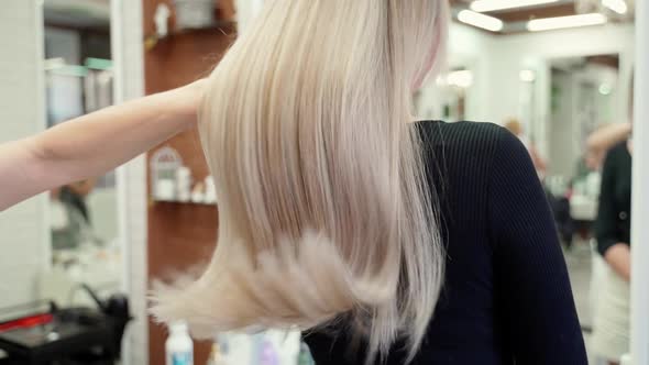 the Hairdresser Runs His Hand Through the Long Beautiful Blond Hair of a Young Woman