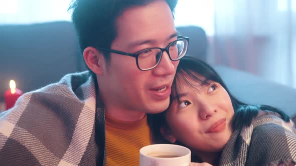 Happy Young Couple Drinking Tea Covered with Blanket with Lights of Candles and Watching Movie