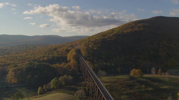 Aerial of sunlight falling on green valley landscape and railroad bridge